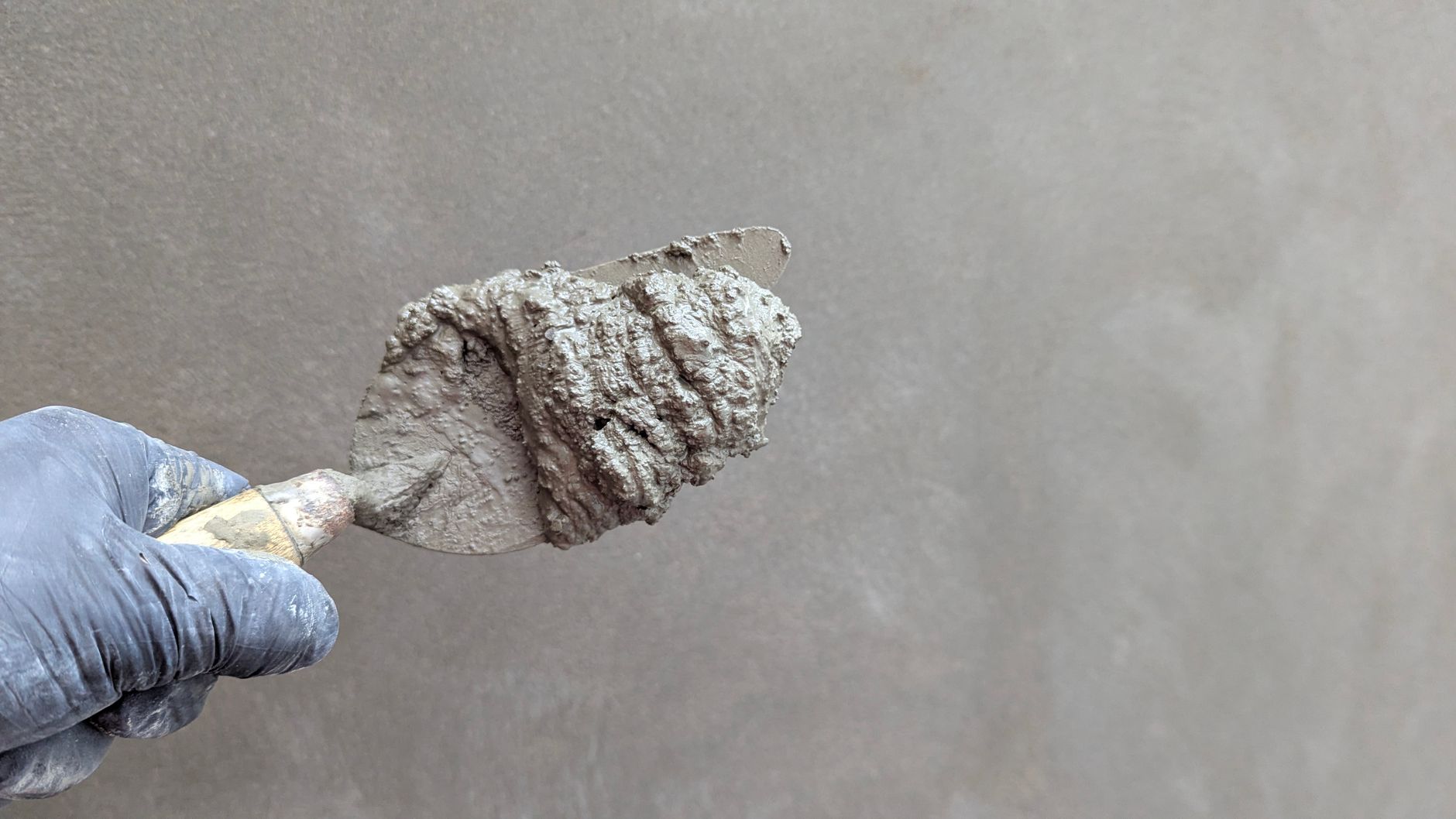 Gloved hand holding a trowel loaded with concrete repair mortar