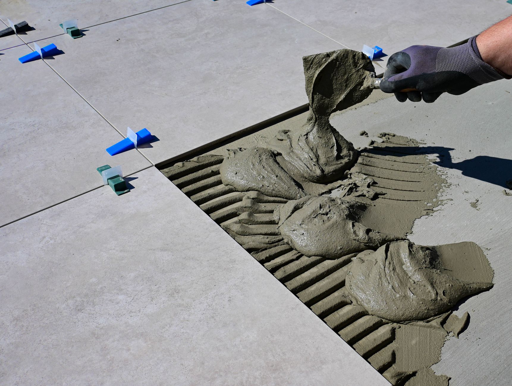 Installer spreading adhesive mortar while laying large floor tiles